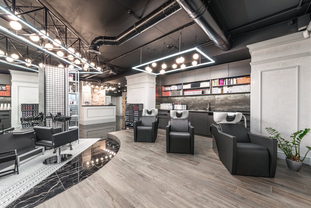 Comfortable backwash chairs with sinks near potted plant placed in contemporary beauty salon with bright illumination and abundance of cosmetology products