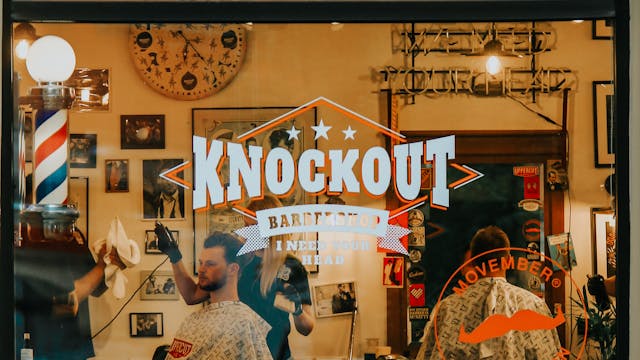 Exterior view of a bustling barber shop in Riga with customers getting haircuts.
