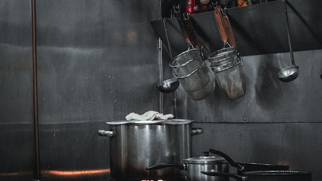 Stainless steel commercial kitchen setup with pots, strainers, and utensils hanging on a rail.
